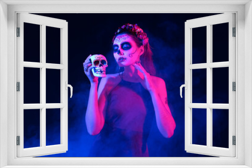Fototapeta Naklejka Na Ścianę Okno 3D - Young woman with painted face and sugar skull for Mexico's Day of the Dead (El Dia de Muertos) on dark background