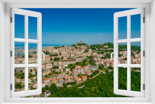 Fototapeta Naklejka Na Ścianę Okno 3D - Aerial view of San Marino old town with old buildings and red roofs on the hill on a sunny day with clear sky. Picture from above with Italy behind in horizon