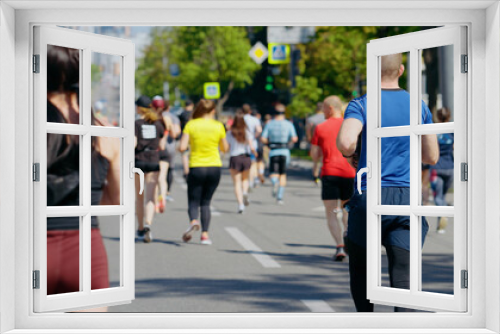 Contestants of city marathon running on asphalt road, focus on woman with ponytail, buildings on blurred background. Back view athletic people taking part in sports competition