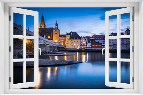 View from the Danube on the Regensburg Cathedral and Stone Bridge with lights in Regensburg in the evening, Germany