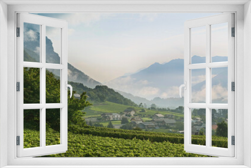 Fototapeta Naklejka Na Ścianę Okno 3D - A greenery scenic of French vineyard with a small village surrounded by mountain alps and greenery with fog in the morning  and dramatic sky