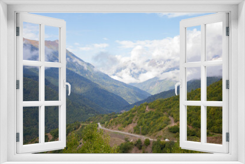 Fototapeta Naklejka Na Ścianę Okno 3D - Summer mountain landscape in the Caucasus mountains. Mountain road. Green Forest. Blue sky with clouds covering the peaks of the mountains. A tourist route.