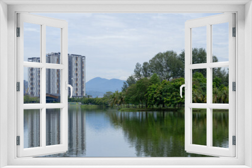Fototapeta Naklejka Na Ścianę Okno 3D - peaceful scene of cityscape in Kepong, Kuala Lumpur, Malaysia. Greenery woods, high-rise buildings, hills and clear cloud sky in background with reflection on water. 