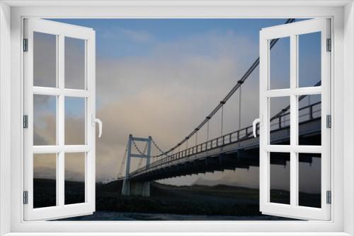 Fototapeta Naklejka Na Ścianę Okno 3D - Wired bridge over a river with cloudy pastel sky in horizontal shot.