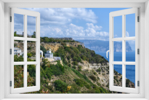 Fototapeta Naklejka Na Ścianę Okno 3D - View of the ancient monastery on a picturesque rock covered with green plants and the Black Sea. Mountains in the distance in the haze. Summer sunny day. Golden domes glisten in the sun. Crimea