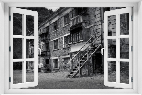 Fototapeta Naklejka Na Ścianę Okno 3D - Black and white photo of old abandoned building in ruined by mudflow small town high in mountains with intricate stonework, ruined balconies, crashed windows. Desolation and destruction