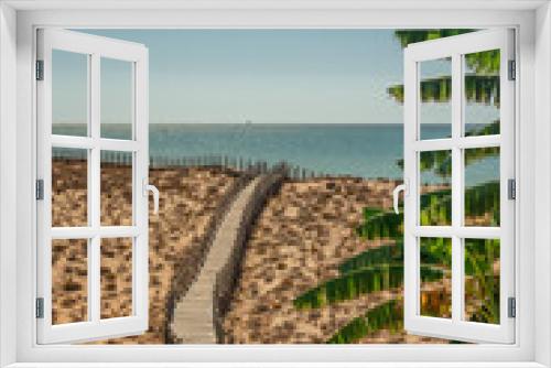 Fototapeta Naklejka Na Ścianę Okno 3D - A romantic seascape of dunes, with palms and a wooden walkway, overlooking the sea. Copy space. Portugal Spain.