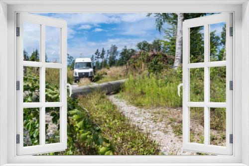 Fototapeta Naklejka Na Ścianę Okno 3D - Van auto standing on impassable dirt road with lying beech trunk fallen in gale. Uprooted tree blocking a forest way with white car or green conifers on blue sky background. Nature disaster aftermath.