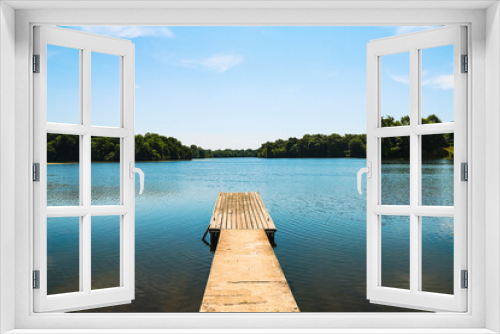 Fototapeta Naklejka Na Ścianę Okno 3D - isolated lonely wooden pier over clam tranquil lake water with trees and blue sky