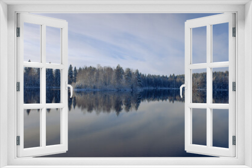 Fototapeta Naklejka Na Ścianę Okno 3D - a snow-covered forest with the first snow, a reflection in the lake against the background of a blue sky with clouds