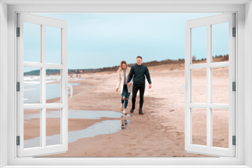 Fototapeta Naklejka Na Ścianę Okno 3D - Attractive young couple walking along the shore of a sandy beach, on a spring romantic holiday, outdoors.