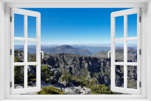 Fototapeta Naklejka Na Ścianę Okno 3D - The top of Table Mountain in Cape Town against the blue sky. Fynbos grows among the picturesque cracked stones. Clouds in the distance. South Africa