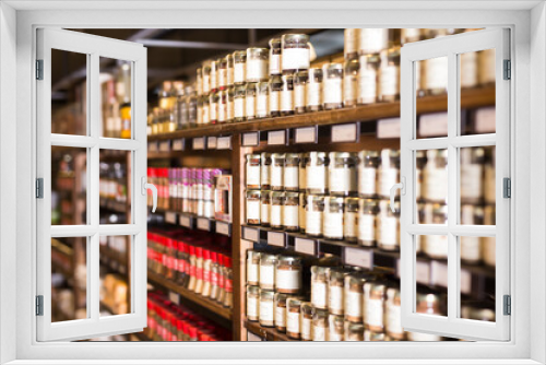 Rows of glass jars with natural spices and herbs lined up on shelves in grocery store