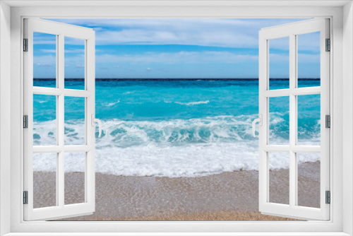 Fototapeta Naklejka Na Ścianę Okno 3D - Azure vibrant waves with white foam and blue sky on sunny coast of Greek island. Sandy beach in Greece. Summer vacation to Ionian Sea