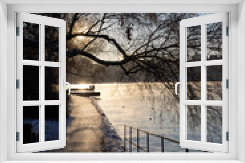 Fototapeta Naklejka Na Ścianę Okno 3D - People walking on a walking path at Stockholm bay on freezing winter day with steaming water, birch tree in front and cozy sun light. Winter time in capital of Sweden  