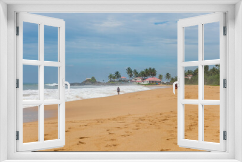 Fototapeta Naklejka Na Ścianę Okno 3D - Asia. Sri Lanka. Ahungalla Beach. People walk along the sea with waves. Yellow sand. Blue sky. Beach houses with tiled roofs and palm trees.