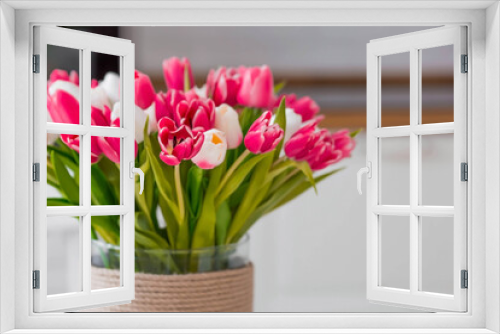 Fototapeta Naklejka Na Ścianę Okno 3D - A bouquet of tulips on a white table. In the background, the interior of a white kitchen in the Scandinavian style. The concept of home comfort.The concept of International Women's Day on March 8.