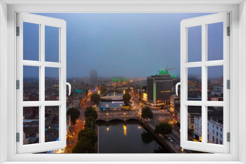 Fototapeta Naklejka Na Ścianę Okno 3D - Aerial view of foggy skyline of Dublin with river flowing with bridge connecting two sides of street surrounded by buildings during a cloudy sunrise morning with illuminated lights