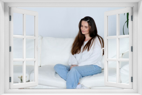 Positive woman in casual clothes sits on comfortable sofa