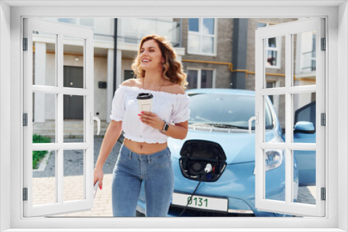 Charging car. Young woman in casual clothes with her electromobile outdoors at daytime