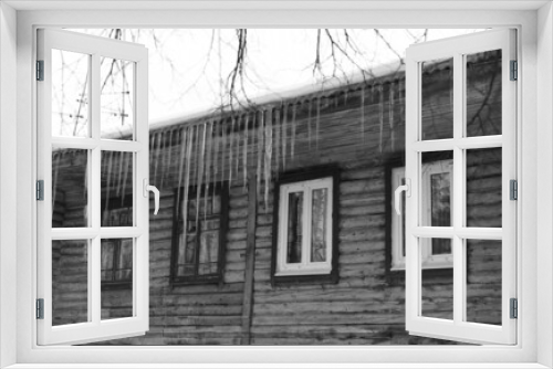 Fototapeta Naklejka Na Ścianę Okno 3D - Long icicles hang from the roof of a wooden house to the very windows.