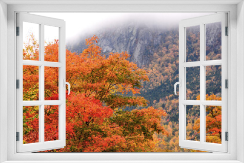 Fototapeta Naklejka Na Ścianę Okno 3D - Colorful fall foliage and steep cliff face of Cannon Mountain partially hidden by low clouds. Located in scenic Franconia Notch State Park, Cannon mountain is a popular destination for rock climbers.