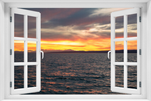 Fototapeta Naklejka Na Ścianę Okno 3D - Twilight at Lake Neusiedl with sun reflections in the water, with cloudy orange-red blue sky. In the background the silhouette of the mountains and rippled water. Calming mood.