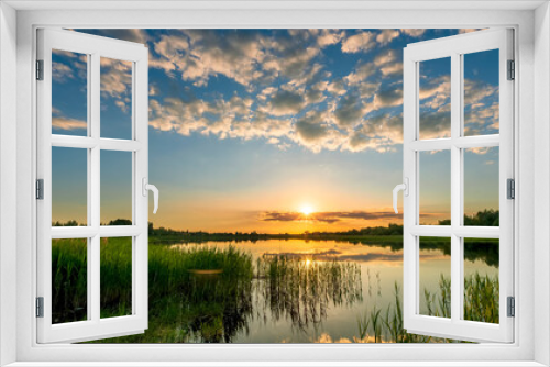 Fototapeta Naklejka Na Ścianę Okno 3D - Amazing view at scenic landscape on a beautiful lake and colorful sunset with reflection on water surface among green reeds and glow on a background, spring season landscape