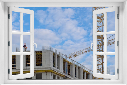 Fototapeta Naklejka Na Ścianę Okno 3D - Close-up view of construction of a modern building. A construction worker in a helmet and an orange special vest stands on top and monitors the progress of work.