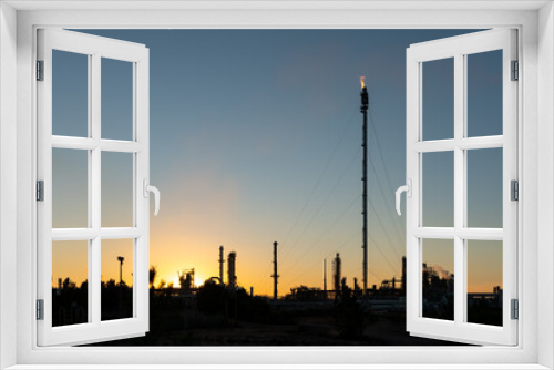 Sines refinery, Portugal at sunset with chimneys giving off flames and smoke.