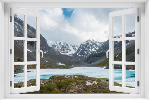 Fototapeta Naklejka Na Ścianę Okno 3D - Atmospheric highland landscape with frozen alpine lake and high snowy mountains. Awesome scenery with icy mountain lake on background of large snow mountains in low clouds. Scenic view to ice lake.