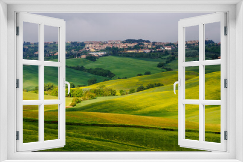 Fototapeta Naklejka Na Ścianę Okno 3D - Spring Tuscany. View of the green fields lit by the rays of the sun. In the distance you can see the city of San Quirico d'Orcia