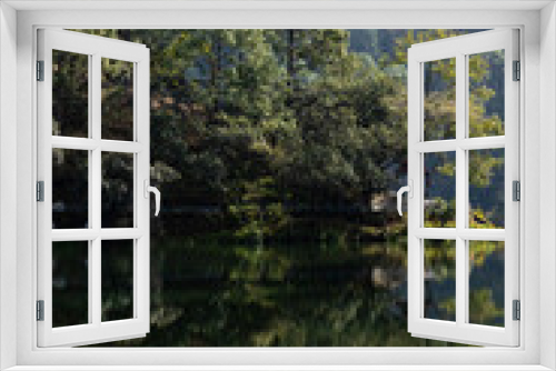 Fototapeta Naklejka Na Ścianę Okno 3D - View of Reflection of dense trees falling on water of a lake at the foothills of a mountain 