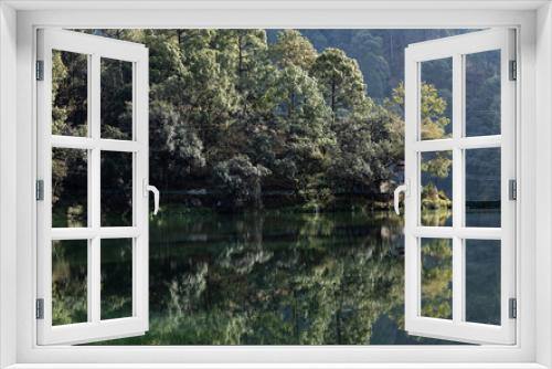 Fototapeta Naklejka Na Ścianę Okno 3D - View of Reflection of dense trees falling on water of a lake at the foothills of a mountain 