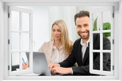 Young attractive man and woman working with papers and laptop in modern office. Blonde girl making notes on paper documents while working with a laptop