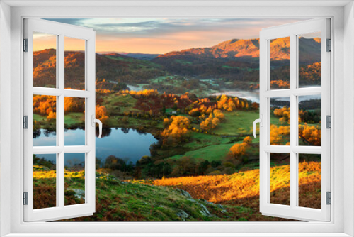 Fototapeta Naklejka Na Ścianę Okno 3D - Wide panoramic view of small lake and mountains with beautiful golden sunrise light on landscape. Loughrigg Tarn, Lake District, UK.