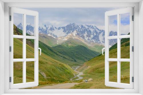 Fototapeta Naklejka Na Ścianę Okno 3D - Mountain valley near Ushguli medieval fortified village in Svanetia, Georgia. Green and grassy mountain slopes, grey rocky cliffs, snow covered summits, sky with clouds, winding road