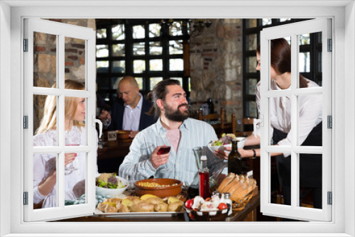 Hospitable young female owner of rustic restaurant serving traditional meals to guests