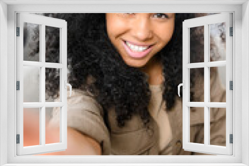 Smiling young multiracial teenage girl sitting on couch in the living room, video-calling via mobile phone, talking to friend, family, taking selfie for social media, staying connected during pandemic