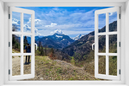 Fototapeta Naklejka Na Ścianę Okno 3D - Man with backpack and scenic view of snow capped mountain peaks of Karawanks near Sinacher Gupf in Carinthia, Austria. Mount Hochstuhl (Stol) visible through forest in spring. Rosental sunny day. Awe