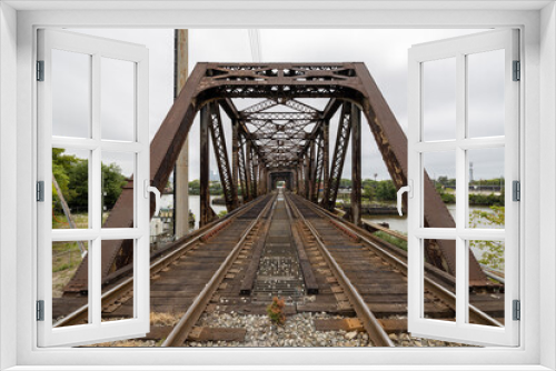Fototapeta Naklejka Na Ścianę Okno 3D - Two railroad train tracks lead into a rusty metal trestle bridge crossing the Schuylkill River in Philadelphia, Pennsylvania, USA