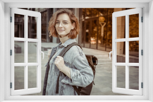 Modern young student woman in stylish denim jacket and backpack outdoors