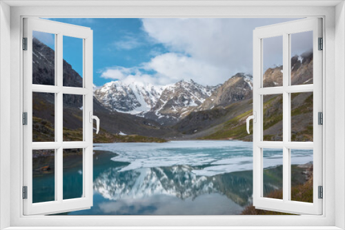 Fototapeta Naklejka Na Ścianę Okno 3D - Atmospheric landscape with frozen alpine lake and high snow mountains. Ice floats on transparent water surface of mountain lake. Awesome scenery with large snowy mountains reflection in clear lake.