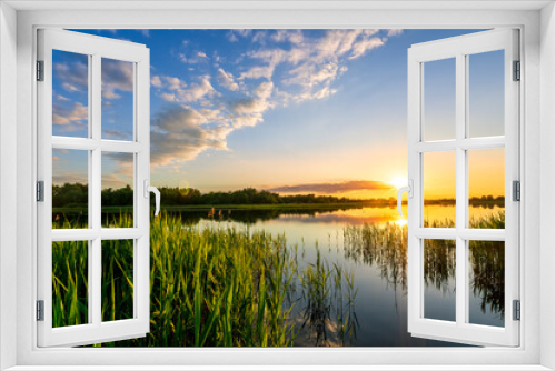 Fototapeta Naklejka Na Ścianę Okno 3D - Amazing view at scenic landscape on a beautiful lake and colorful sunset with reflection on water surface among green reeds and glow on a background, spring season landscape