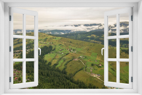 Green slopes of Ukrainian Carpathian mountains in summer. Cloudy morning, low clouds. Aerial drone view.