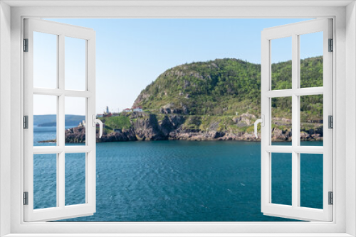 Fototapeta Naklejka Na Ścianę Okno 3D - A summer's scene of St. John's, Newfoundland at sunset. The sky is pink and blue. There's a lighthouse at the land's point along with small homes.  The bottom part of the picture has a marine marker  