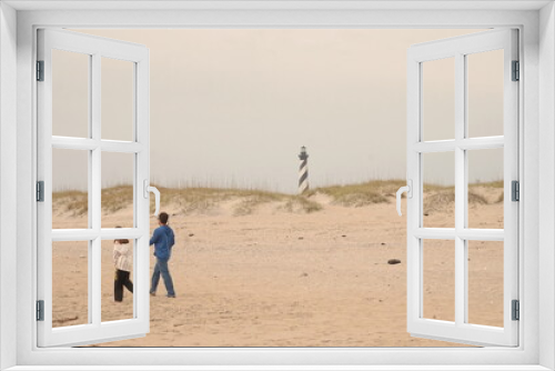 Fototapeta Naklejka Na Ścianę Okno 3D - Couple Walking on the Beach in Front of Dunes and Cape Hatteras Lighthouse in Daylight