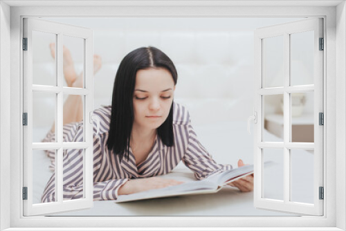 Barefoot young teenage girl lying on her bed reading a book or studying