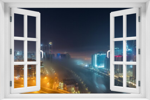 Fototapeta Naklejka Na Ścianę Okno 3D - Buildings are covered in thick layer of fog in Business Bay night timelapse.