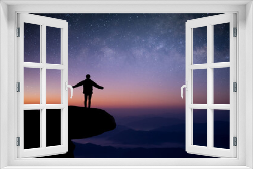 Fototapeta Naklejka Na Ścianę Okno 3D - Silhouette of young traveler standing and open arms alone on top of the mountain and watched the beautiful view night sky, star and milky way. He was happy to travel alone in the wide world.